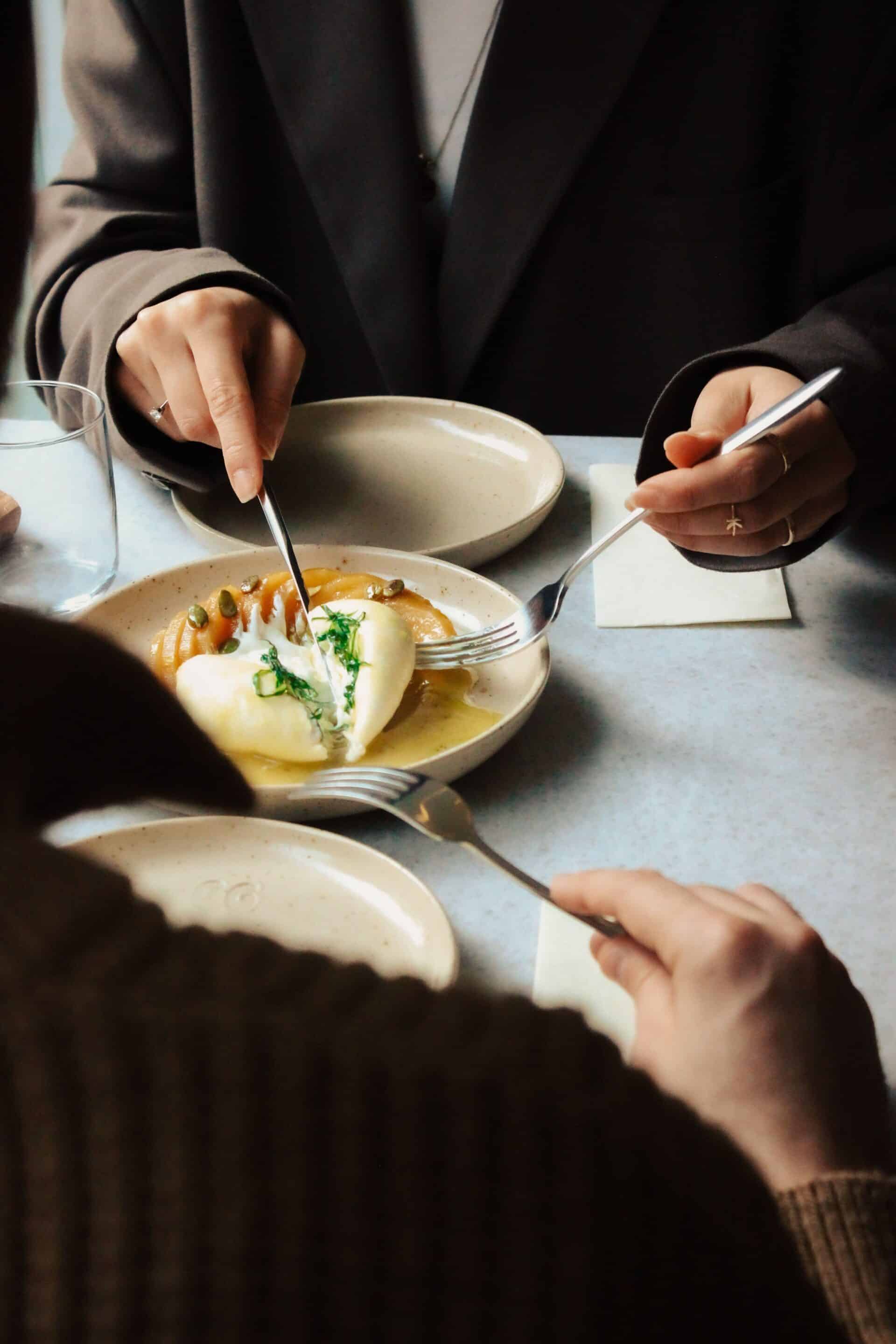 Two adults enjoying a shared gourmet dish at a stylish cafe table with natural light.